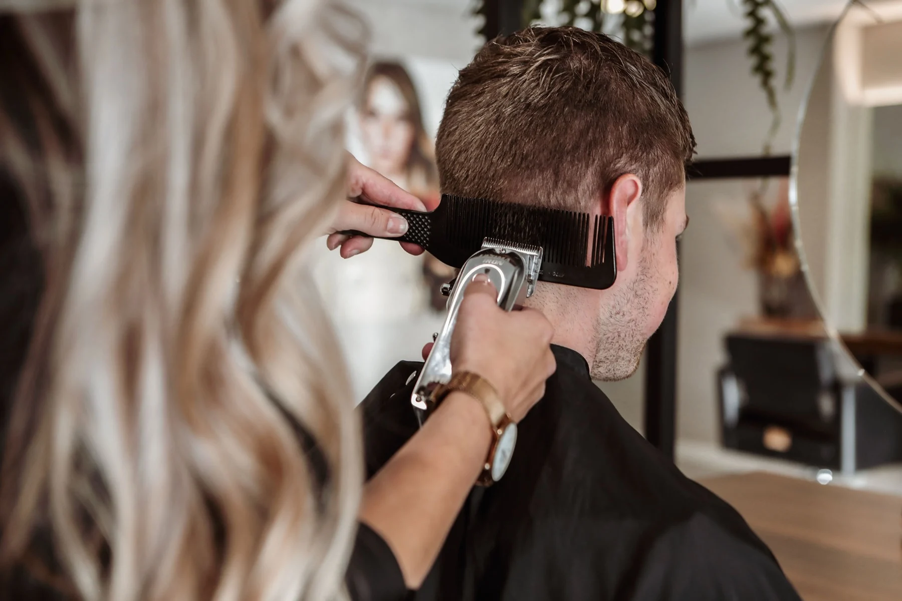 Hairstylist werkt de nek van een heer bij met een tondeuse en kam