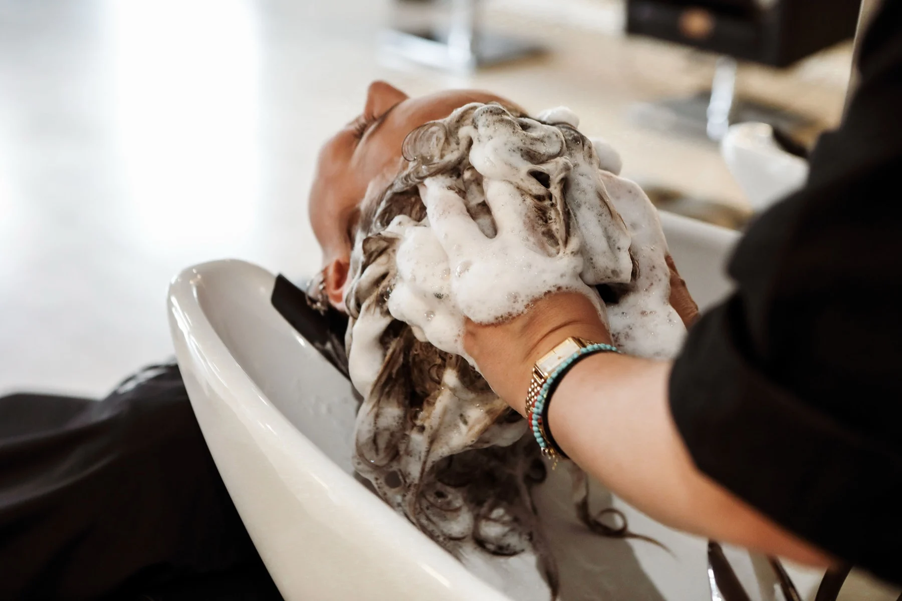 Een klant krijgt een haarwasbeurt bij de wasbak