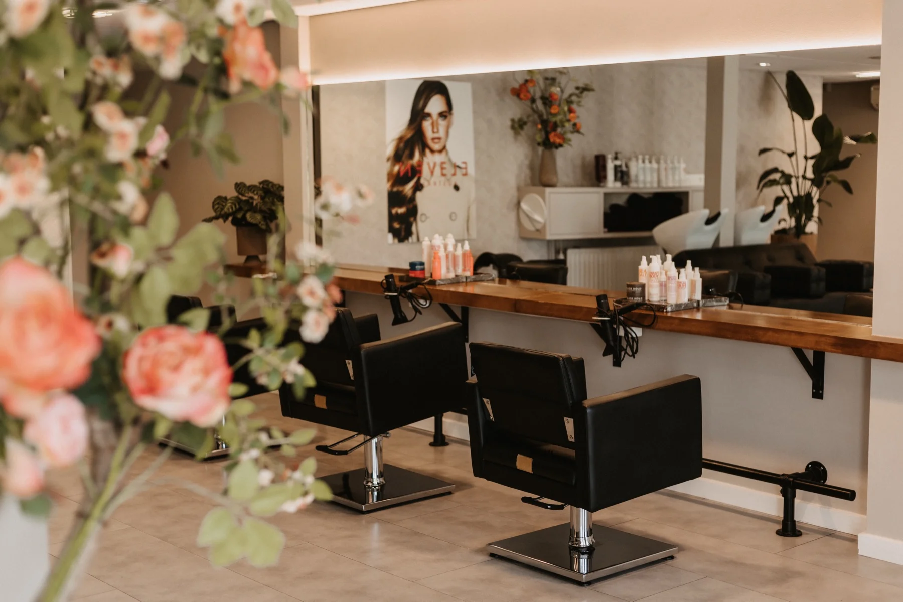 Het interieur van LOOX Kappers met kappersstoelen, spiegels en roze bloemen op de voorgrond